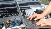 Männerhände an Laptop auf dem Motor eines Autos