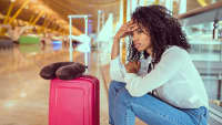 Frau sitzt mit ihrem Koffer am Flughafen