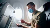 Ein Mann sitzt im flugzeug mit einer vorgeschriebenen OP Maske als Mund Nasenschutz