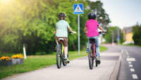 zwei Kinder fahren auf dem Gehweg mit dem Rad