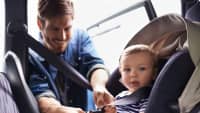 Mann schnallt Kleinkind in Kindersitz im Auto fest