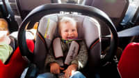Kleinkind sitzt lachend im Kindersitz auf der Rücksitzbank eines Autos