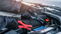 Mann mit Handschuhen schließt Starterkabel für eine Autobatterie an