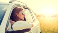 Frau mit Sonnenbrille schaut aus einem Auto in die Sonne