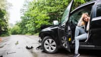 Junge Frau sitz mit Handy im  Auto nach einem Unfall