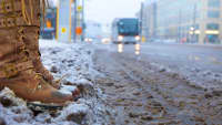 Frau steht im Winter am Straßenrand während sich ein Bus nähert