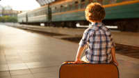 Ein Junge sitzt am Bahnhof ganz alleine auf einem Koffer