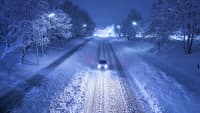 ein Auto fährt Nachts auf verschneiter Strasse
