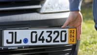 Ein Mann befestigt an einer Prägestelle in Bad Oldesloe ein Kurzzeitkennzeichen an einem Auto.