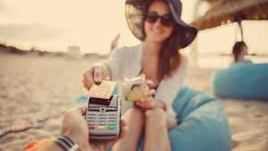 Eine Frau sitzt am Strand und bezahlt ihren Cocktail mit einer debitkarte oder kreditkarte