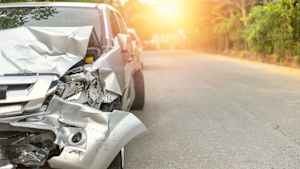 Beschädigtes silberes Auto bei Sonnenuntergang nach einem Unfall mit dem Leasingauto