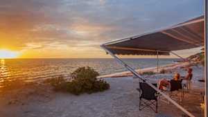 Ein Mann und eine Frau genießen an einem Strand den Sonnenuntergang, denn in man kann jetzt in Australien Camper mieten