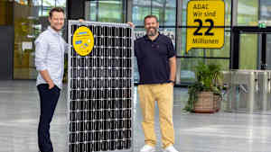 Zwei Männer halten ein Solarpanel aufrecht in dem Foyer eines Gebäudes und verdeutlichen so die Zusammenarbeit zwischen adac und otovo.