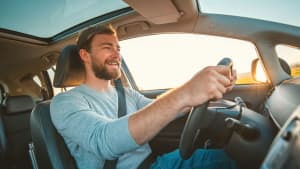 Mann sitzt bei Sonnenuntergang lächelnd hinter dem Steuer eines Autos, weil er sich vor der Auto Anschaffung gut informiert hat