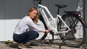 Eine Frau kniet vor einer Garage  neben einem weißen Flyer Fahrrad der Generation E und lädt dieses.