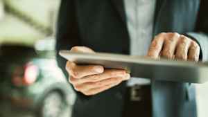 Eine Person im Anzug hält ein Tablet, um seine Autofinanzierung zu organisieren.
