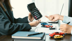 Eine Person präsentiert einen Taschenrechner, eine andere Person füllt ein Formular aus zum Auto finanzieren