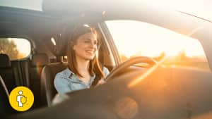 Frau sitzt hinter dem Steuer eines Autos bei Sonnenuntergang und lächelt, weil sie durch die GAP-Versicherung beim Leasing total abgesichert ist.