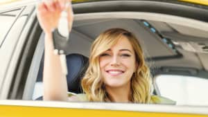 Frau, die Vorteile und Nachteile des Auto leasing kennt, hält Schlüssel aus dem Fenster eines gelben Autos