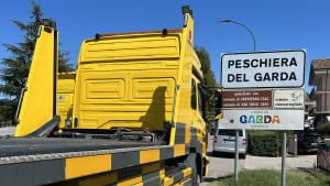 Ein ADAC-Transporter neben einem Ortsschild des Gardasees und ist bereit für einen Fahrzeugrücktransport