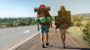 Zwei Rucksacktouristen gehen am Rande einer Straße entlang und sind unbeschwert, weil sie einen ADAC Auslandskrankenschutz Langzeit haben