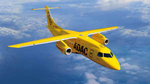 Ein leuchtend gelbes ADAC-Ambulanzflugzeug vom Typ Dornier 328, das über einer Wolkendecke fliegt und jemanden,der krank im urlaub ist, abholt.
