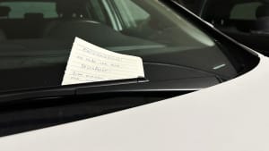 Unter den Scheibenwischer eines weißen Autos wurde ein handschriftlicher Zettel gesteckt