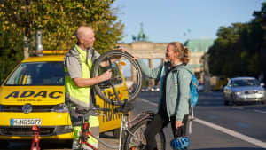 Ein Pannenhelfer des ADAC repariert das Fahrrad einer Frau auf einer Strasse vor dem Brandenburger Tor in Berlin