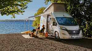 Menschen sitzen vor ihrem Wohnmobil an einem See