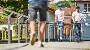 Zwei E-Scooter fahre auf einem Bürgersteig rücksichtslos nah an einme Fußgänger vorbei