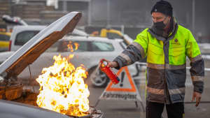 Ein Mann löscht mit dem Handfeuerlöscher einen Brand im Motorraum