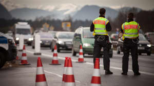 Zwei Polizisten stehen auf der Autobahn und kontrollieren an der Grenze von Deutschland zu Österreich.