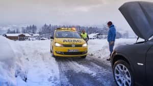 Ein Pannenfahrzeug vom ADAC kommt zu einem havarierten Fahrzeug. Es ist Winter und liegt viel Schnee.