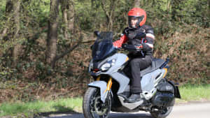 Der hellgraue Motorroller Peugeot XP400 GT während der Fahrt, seitlich von vorne fotografiert