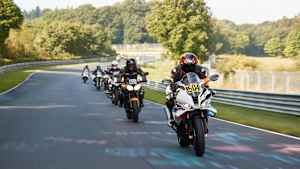 Eine Gruppe von Motorradfahrern fährt auf einer Straße, umgeben von Bäumen und grüner Landschaft.