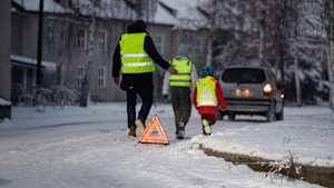 Ein Vater und seine zwei Kinder haben eine Autopanne. Sie laufen mit Warnwesten vom Warndreieck zurück zum Auto