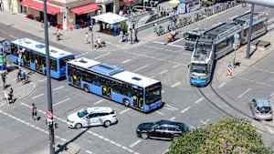 Verschiedene Verkehrsteilnehmer wie Autofahrer, Straßenbahn, Bus, Fußgänger und Radfahrer fahren über eine Kreuzung