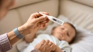 Ein kleines Kind liegt & die Mutter hält gerade ein Fieberthermometer in der Hand