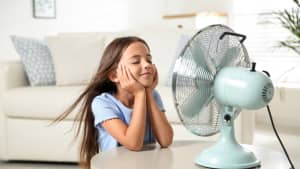 Ein Mädchen lässt sich vom Ventilator kühlen Wind ins Gesicht pusten