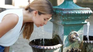 Eine Frau trinkt aus einem öffentlichen Brunnen Wasser