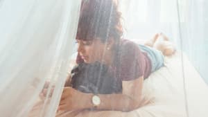 Eine Frau sitz auf dem Bett unter Mückennetz