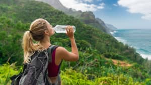 Frau trinkt auf einer Wanderung am Meer aus einer Flasche