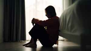 Eine junge frau mit Depressionen sitzt im Schlafzimmer auf dem Boden.