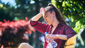 Junge Frau sitzt mit einer Wasserflasche in der Hand auf einer Parkbank