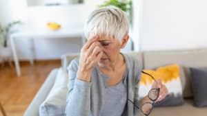 Ältere Frau reibt sich die Augen und hält dabei ihre Brille in der anderen Hand