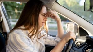 üde junge Autofahrerin, die an Kopfschmerzen und Migräne leidet, sitzt am Fahrersitz und berührt die schmerzhafte Stirn.