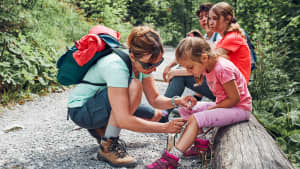 Mutter, die die Wunde auf dem Knie ihrer kleinen Tochter mit sprühmedizinischer Medizin anzieht.