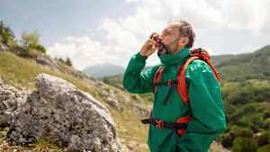 Ein Mann welcher in den Bergen unterwegs ist und an einem Asthmaspray zieht
