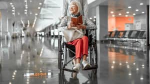 Mann im Rollstuhl holt seinen Koffer vom Gepäckband im Flughafen