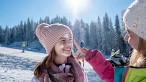 Eine Frau trägt im Winter ihrer Tochter beim Skifahren Sonnenschutz auf